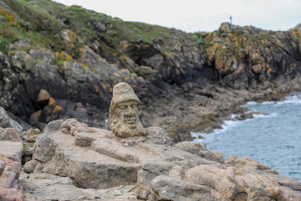 Visage sculptée dans la pierre en bord de falaise, face à la mer