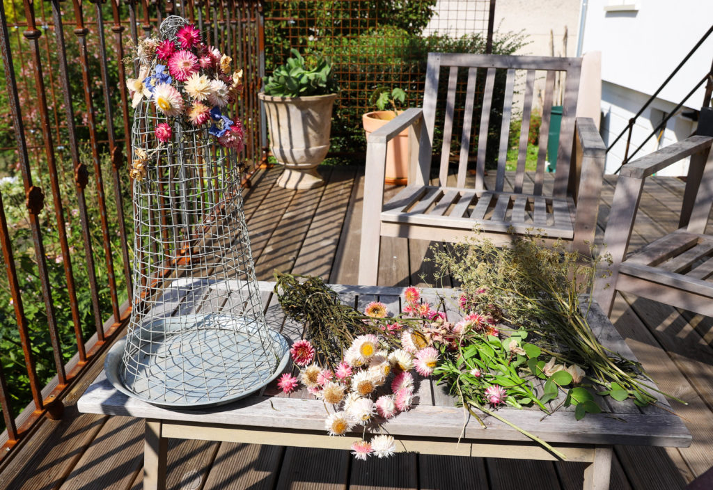 cloche en grillage et des fleurs séchées posées sur une table en bois pour réaliser une composition