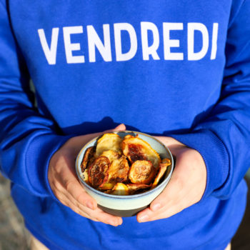 Garçon avec un pull bleu avec inscription VENDREDI tient un bol de chips de courgettes dans ses mains