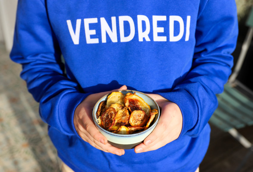 Garçon avec un pull bleu avec inscription VENDREDI tient un bol de chips de courgettes dans ses mains