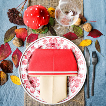 décoration de table d'automne avec une serviette pliée en forme de champignon , des feuilles d'arbres sèches colorées et des noix