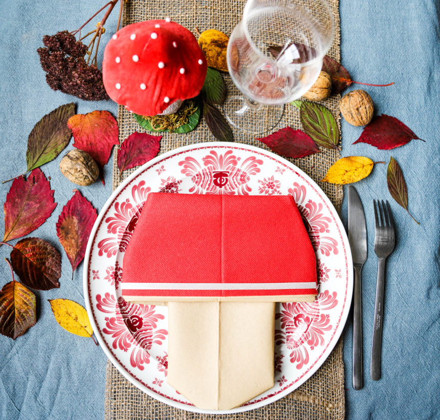 décoration de table d'automne avec une serviette pliée en forme de champignon , des feuilles d'arbres sèches colorées et des noix