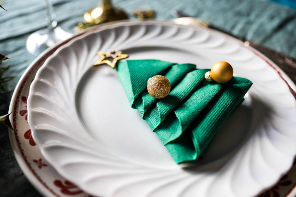 serviette verte pliée en forme de sapin avec des mini boules de Noël dorées